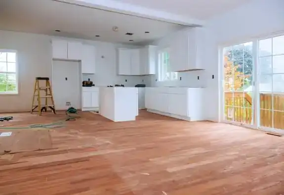 Open-plan interior with a white kitchen and hardwood floors going down