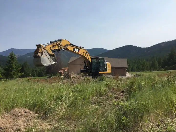 Excavator cutting a driveway on a hillside below the mountains
