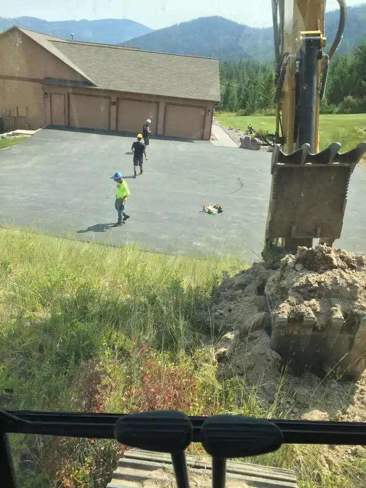 Crew finishing a new slab, seen from above with the excavator bucket in frame