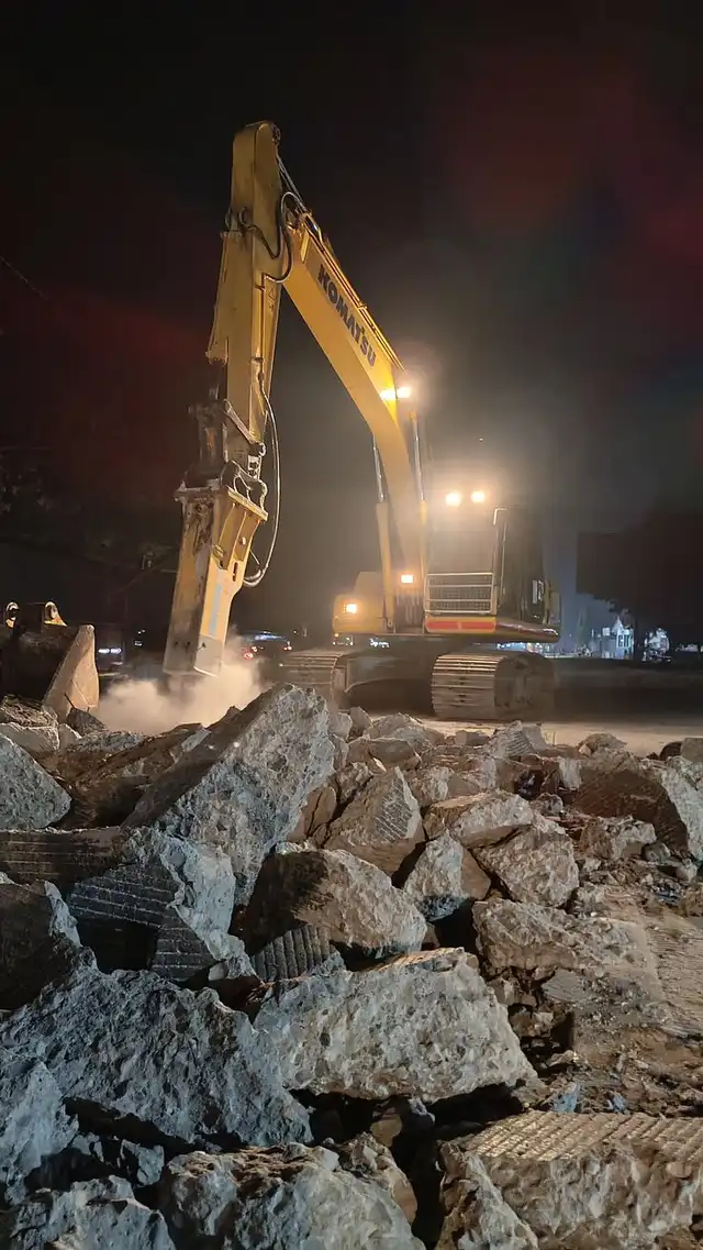 Excavator on demolition rubble at night